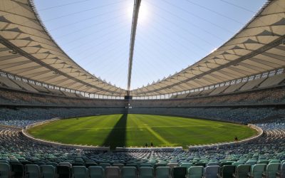 A large stadium with green grass with Moses Mabhida Stadium in the background